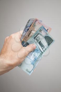 Male hand holding Jordanian dinars banknotes over gray background, vertical photo