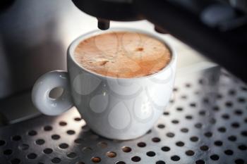 White ceramic cup of fresh espresso with foam in the coffee machine.