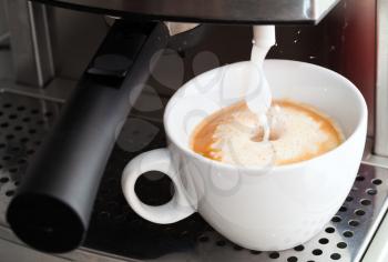 Coffee maker pouring hot milk foam in espresso coffee to prepare cappuccino