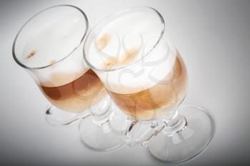 Two glasses with handles of latte coffee on gray background