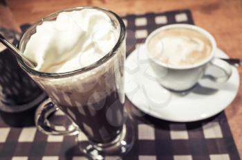 Glass of hot chocolate and cup of cappuccino coffee stand on a table 