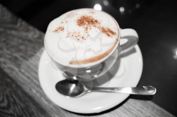 Cappuccino, cup of coffee with milk foam and cinnamon stands on black table in cafeteria, close-up photo, selective focus