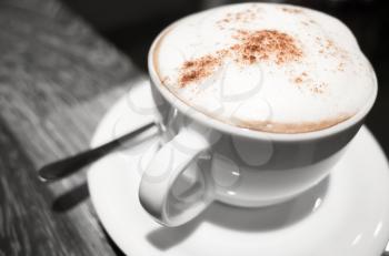 Cappuccino, cup of coffee with milk foam and cinnamon stands on black table in cafeteria, close-up photo with selective focus