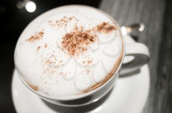 Cappuccino, cup of coffee with milk foam and cinnamon stands on black table in cafeteria, close up photo with selective focus