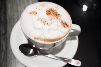 Cappuccino, cup of coffee with milk foam and cinnamon stands on black table in cafeteria, closeup photo with selective focus