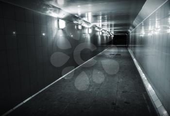 Monochrome photo of underground passage with lights and stairs in dark end