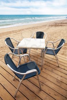 Open space seaside bar interior with wooden floor and metal armchairs on the sandy beach