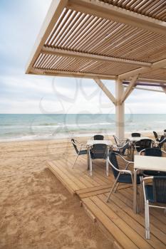 Sea side bar interior with wooden floor and metal armchairs on sandy beach in Spain