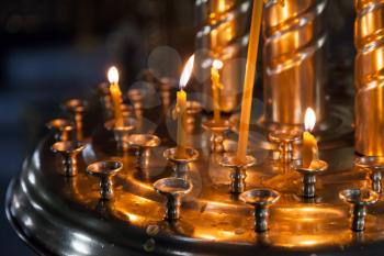 Small candles are lit in a dark Orthodox Church