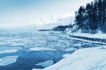 Winter coastal landscape with floating ice and frozen pier. Gulf of Finland, Russia. Blue toned monochrome photo