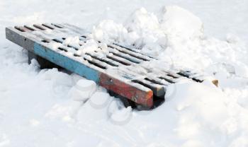 Winter park fragment. Wooden bench in snowdrift