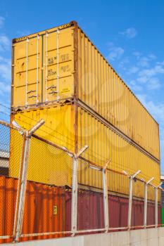Metal Industrial cargo containers are stacked under blue cloudy sky. Vertical photo