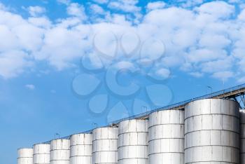 Abstract industrial architecture fragment on blue sky background, shining metal tanks for storage of bulk materials