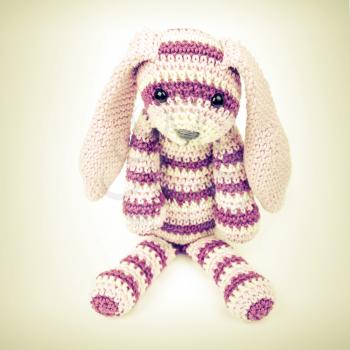 Knitted rabbit toy sitting over white background with soft shadow, vintage toned square photo with retro style toned effect