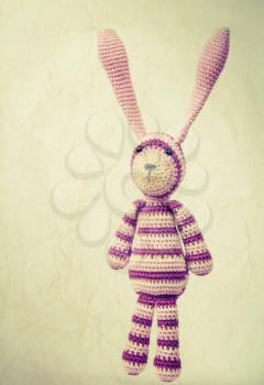Funny knitted rabbit toy portrait with ears up, vintage toned photo with retro style toned effect and old paper texture