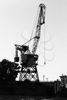 Dark silhouette of industrial port crane. Danube River coast, Bulgaria. Black and white vertical photo