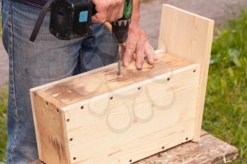 Homemade birdhouse made of wood is under construction, carpenter works with drill