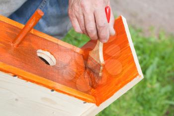 Homemade birdhouse made of wood is under construction, worker adds protective covering with brush