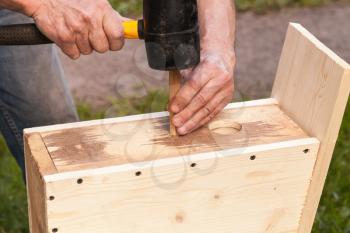 Wooden birdhouse is under construction, carpenter works with rubber hummer