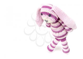 Sad knitted rabbit toy goes over white background with soft shadow, selective focus with shallow DOF