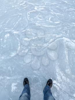 Winter walking on ice, man's legs on frozen sea surface