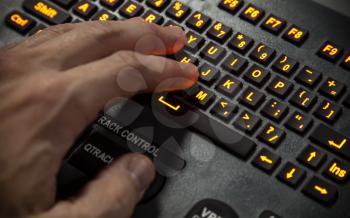Hand on illuminated industrial qwerty keyboard. Selective focus