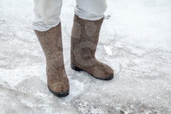 Feet with traditional Russian felt boots on winter road with snow and ice 