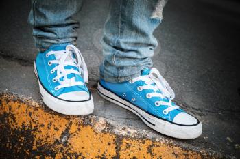Blue sneakers, teenager feet stands on urban roadside. Closeup photo with selective focus and shallow DOF