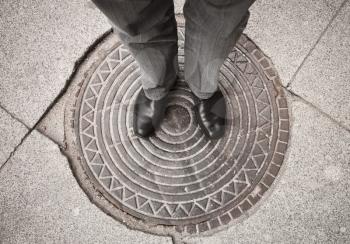 Urbanite man in black new shining leather shoes standing on rusty sewer manhole