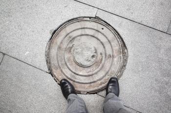 Feet of an urbanite man in black new shining shoes standing on rusty sewer manhole