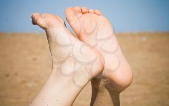Barefoot legs of kid who is lying on the beach in sunlight