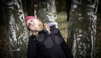 Little beautiful blond girl dreamily leaning on the birch