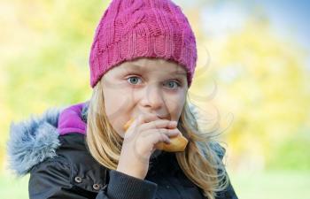 little beautiful blond girl eating cake in autumnal park. Outdoor portrait.