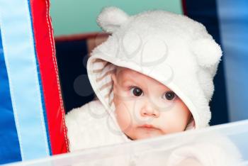 little baby in white bear costume looks through the window on a playground