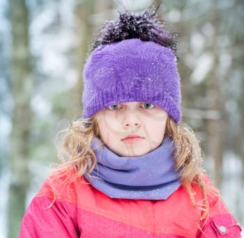 Little blond girl in winter outwear with snowflakes above forest background