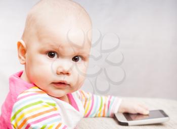 Little baby in colorful striped clothing with mobile phone looks in camera
