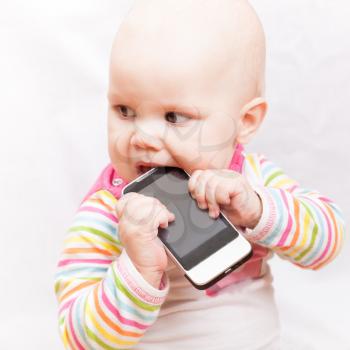 little baby baby chews on a mobile phone in colorful striped clothing