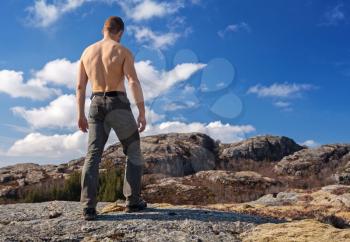 Topless strong man stands on the mountain and looks down