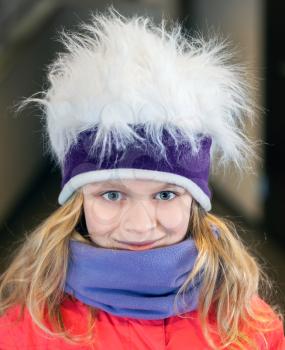 Little blond girl in fun artificial fur hat. Closeup outdoor portrait