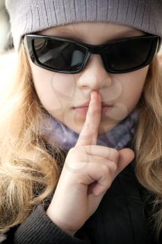 Little girl in black sunglasses shows silence sign