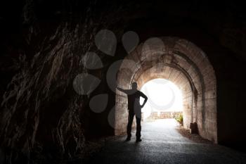 Young man stands relaxed in dark tunnel and looks in the light