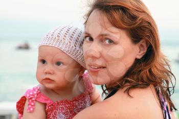 Brown-eyed young Caucasian mother with her baby girl on the sea coast