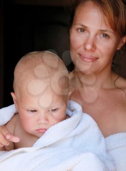 Young Caucasian mother holds her little baby in white cotton towel after the bath