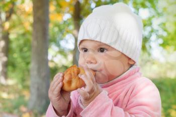 Little Caucasian baby girl in autumn park eats small pie