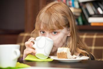 Little blond girl drinks tea with cake