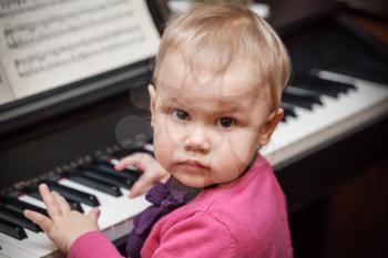 Little baby girl playing music on classical piano