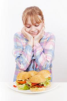 Little smiling blond girl looks on homemade hamburgers on white plate