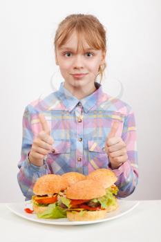 Little blond girl with big homemade hamburgers showing thumbs up