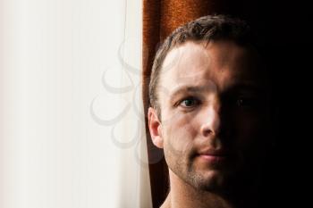 Young Caucasian man near the window, closeup portrait 