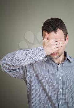 Young sad Caucasian man hiding his face with hand